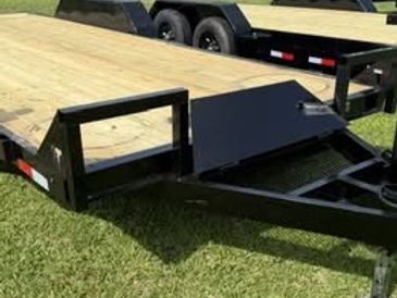 Black flatbed trailer with wooden deck on grass.