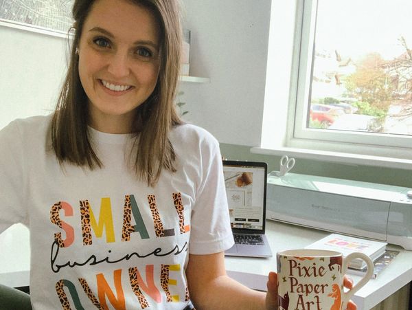 A smiling woman promoting small business with a colorful shirt and a Pixie Paper Art mug.
