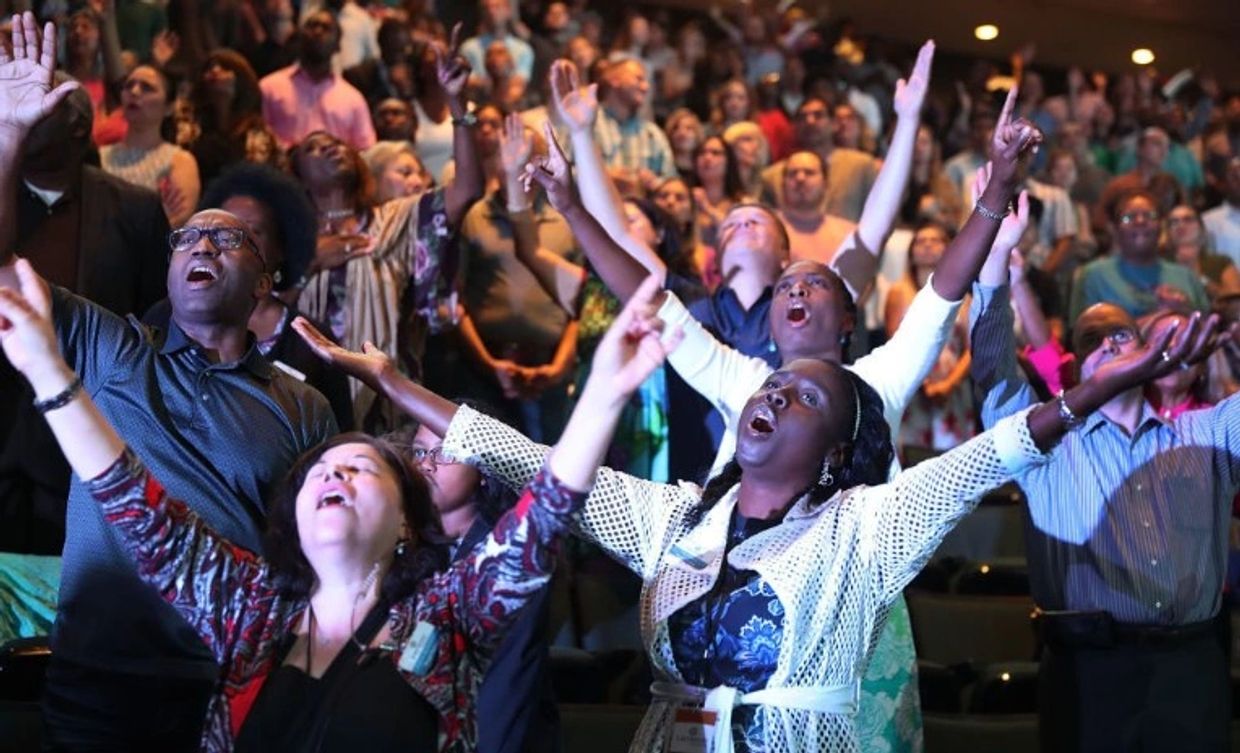 People in a crowd raising their hands, singing or cheering passionately.