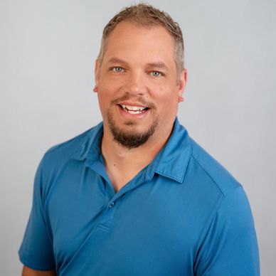 Smiling man in blue polo shirt against a neutral background.