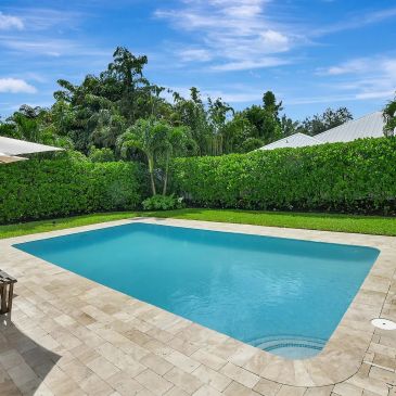 Clear blue pool surrounded by greenery and a patio.