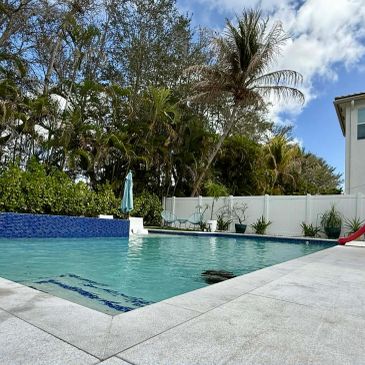 A backyard swimming pool surrounded by trees and a white fence.