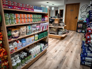 Pet supplies and food neatly arranged in a store with wooden flooring.