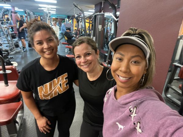 Three smiling women at the gym, posing for a selfie after a workout.
