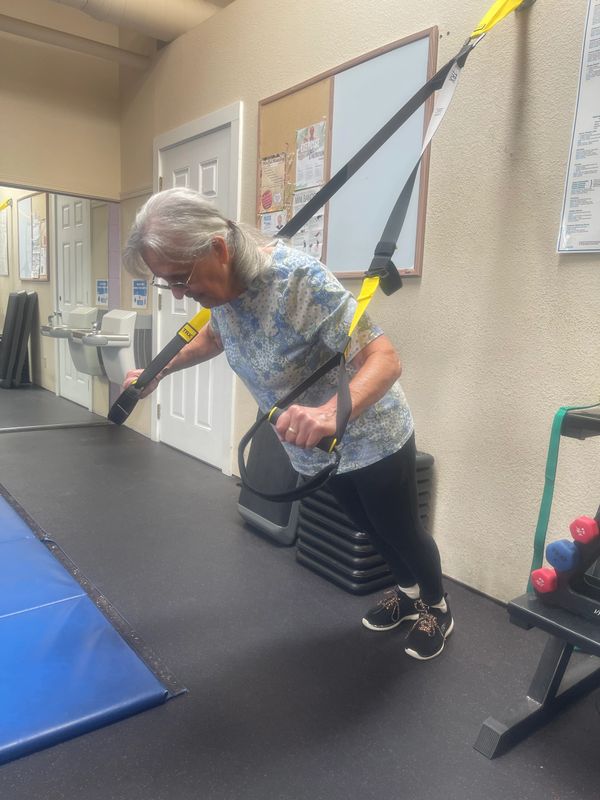 Senior woman exercising with TRX straps in a gym.
