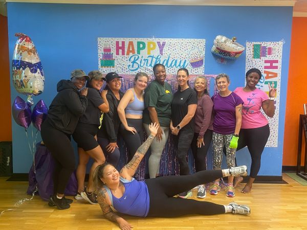Group of women celebrating a birthday with balloons and decorations indoors.