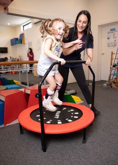 Physiotherapist and child jumping on trampoline to improve gross motor skills