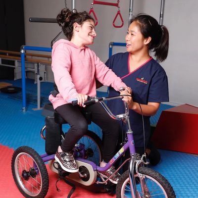 Child on adaptive bicycle assistive technology with paediatric physiotherapist