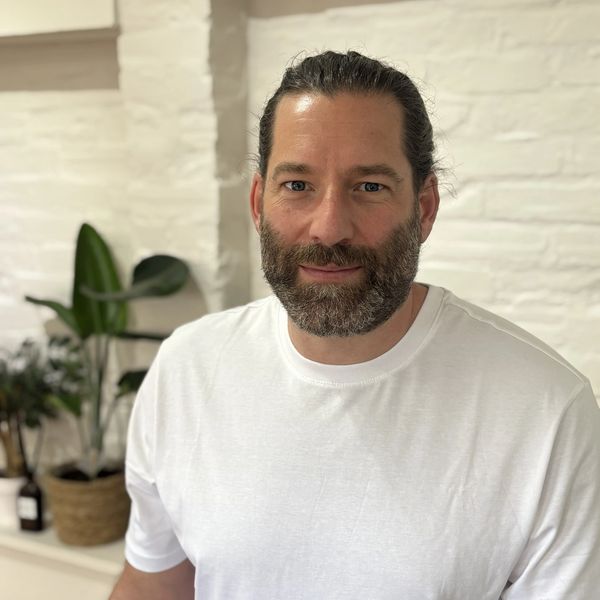 Man with a beard and tied-back hair wearing a white t-shirt indoors.