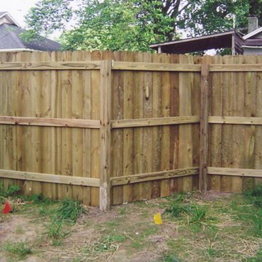 Corner wooden fence in a backyard with grass and houses in the background.