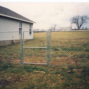 Chain-link fence with a gate beside a house on a cloudy day.