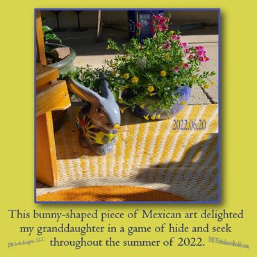 Mexican art bunny planter with blue round planter with yellow and pink flowers on yellow mat