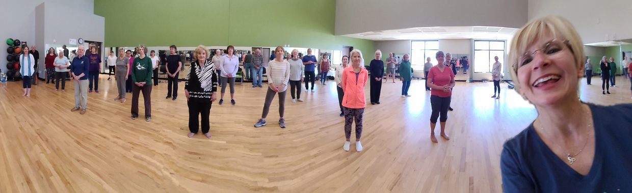 Panoramic view of a group of people in fitness studio for World T'ai Chi Day celebration.