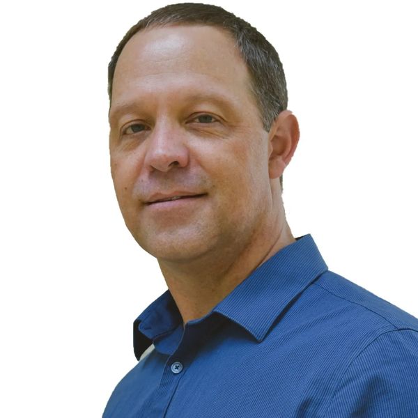 A confident man in a blue shirt smiles slightly against a white background.