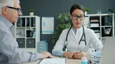 A doctor reviews information on a laptop while consulting with a patient.