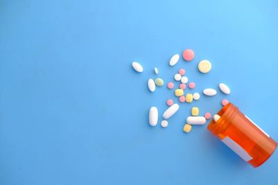 An orange prescription bottle lies on its side with assorted pills spilled onto a blue surface.
