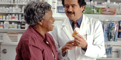 A pharmacist explains a prescription bottle to an older customer at a pharmacy counter.