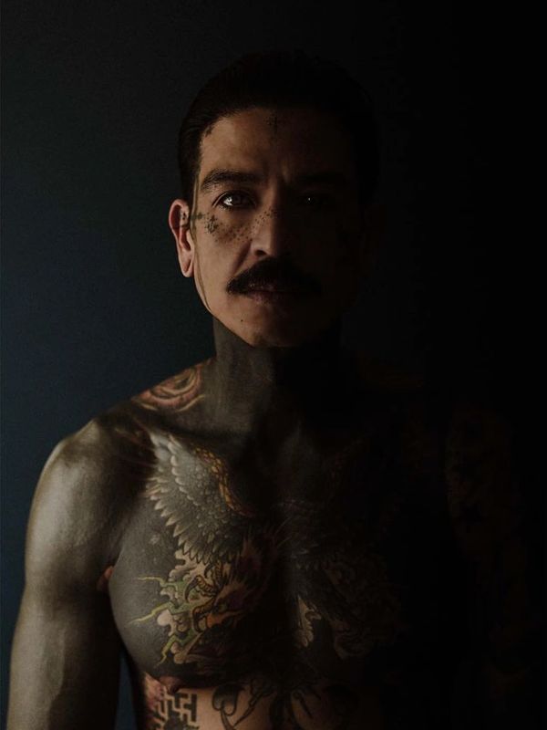Portrait of Charlie Coffin with detailed chest tattoo in dramatic shadow.