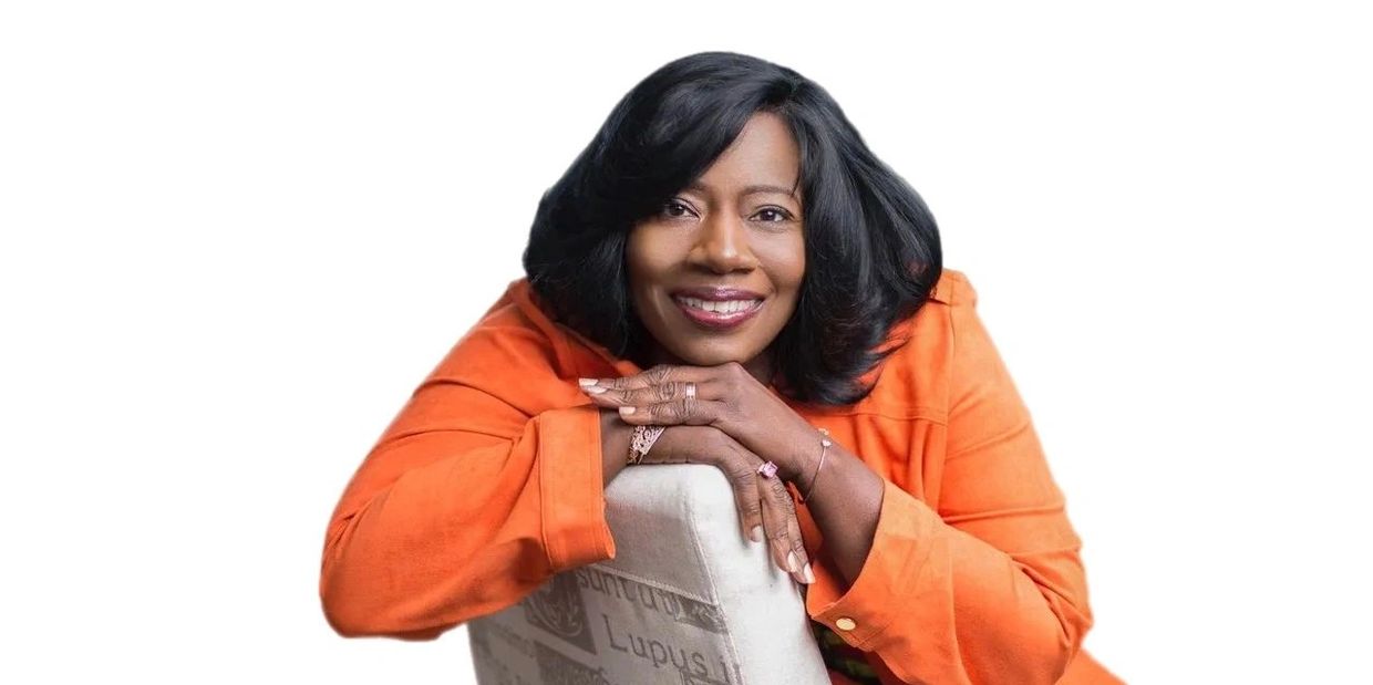 Woman in orange leaning on a chair with a smile.