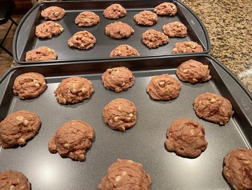 Two trays of freshly baked chocolate cookies on a kitchen counter.