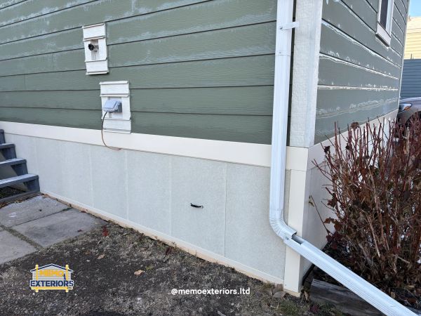 Side view of a house exterior with green siding and a white downspout.