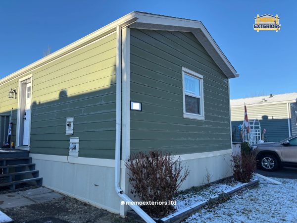 Green exterior siding on a small house with white trim and a clear blue sky.
