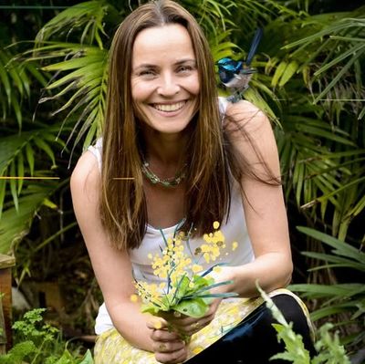 Smiling woman holding flowers in a garden with a bird on her shoulder.