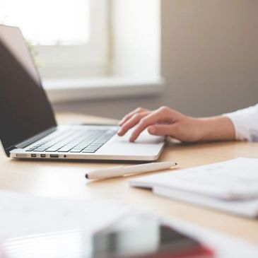 Woman using her computer's touchpad on her desk with a pen and notebook.