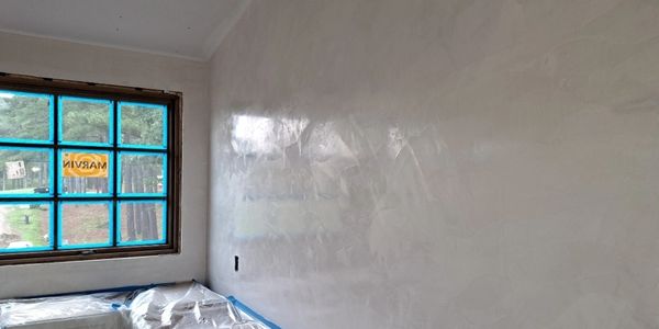 Freshly plastered wall in a kitchen under renovation with plastic-covered counters.