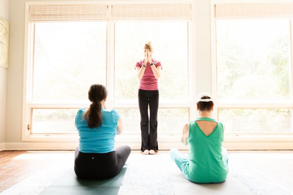 Image of two women sitting on yoga mats with an instructor standing and guiding them in breathwork.