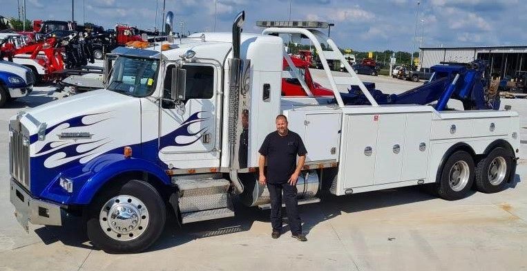Man standing next to a large blue and white tow truck with flame decals.