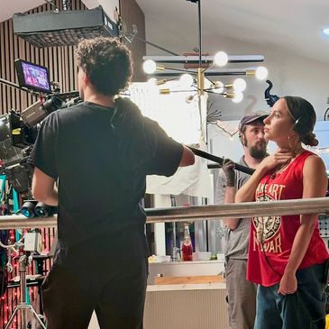 Film crew recording a woman wearing a red sleeveless shirt.