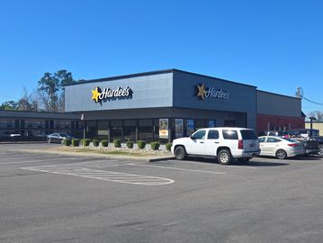 Modern Hardee's restaurant with clear blue sky and parked cars.