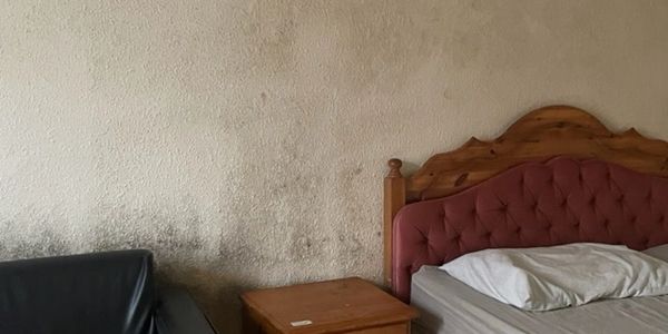 A bedroom with the wall covered in mould