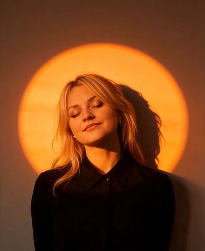 Woman with eyes closed in warm sunlight circle.