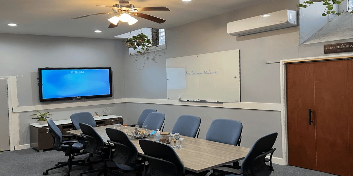 Modern conference room with blue chairs, a wooden table, TV, and whiteboard.