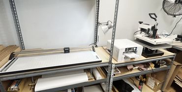 Workspace shelving with cutting board, printer, heat press, and storage items.