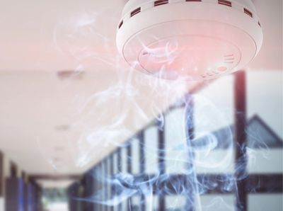 Smoke detector on a ceiling with smoke surrounding it.
