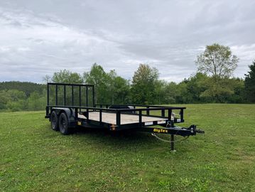 Flatbed utility trailer parked on grassy field under cloudy sky.