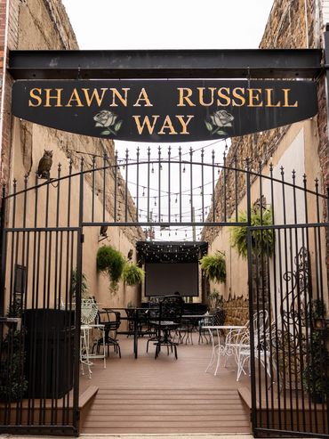 Outdoor seating area named Shawna Russell Way with decorative plants and string lights.