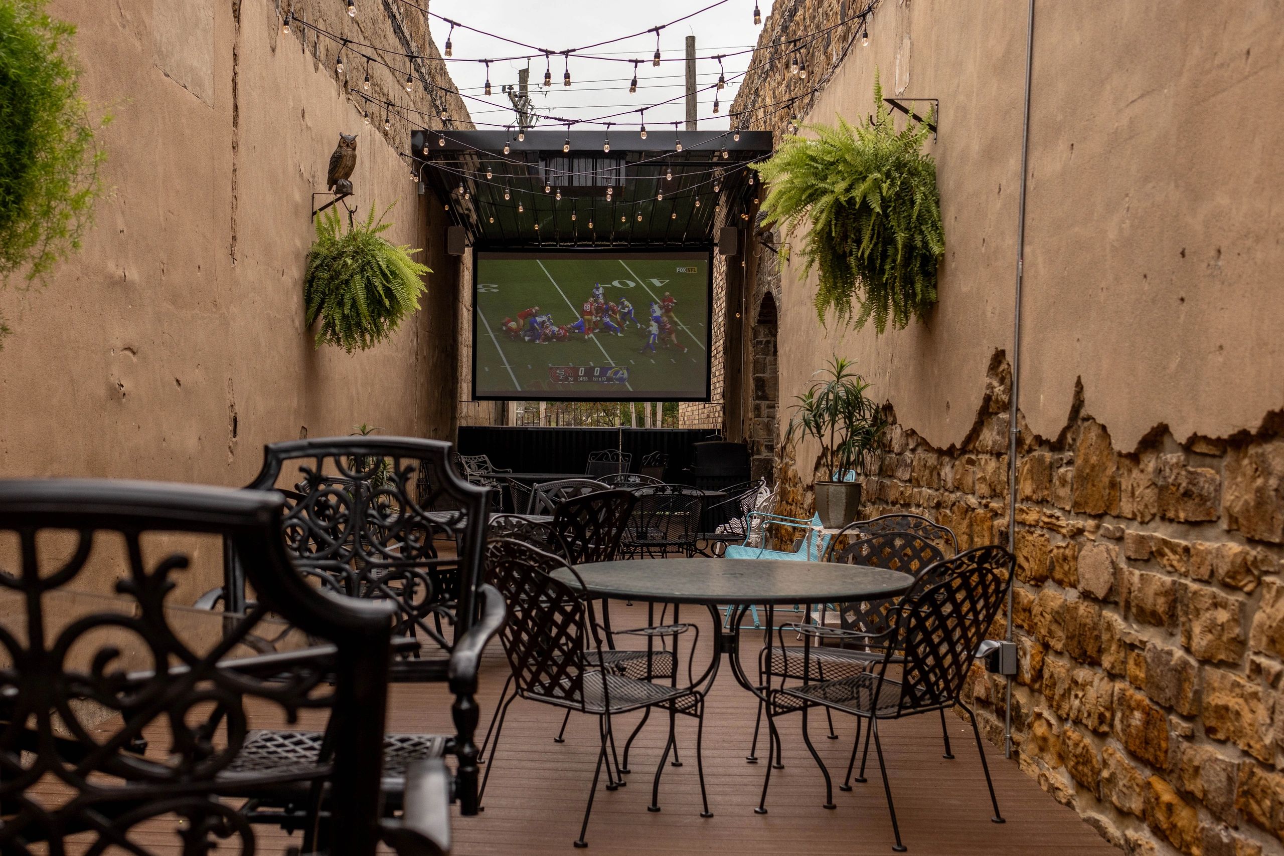 Outdoor seating area with a screen showing a football game and string lights.