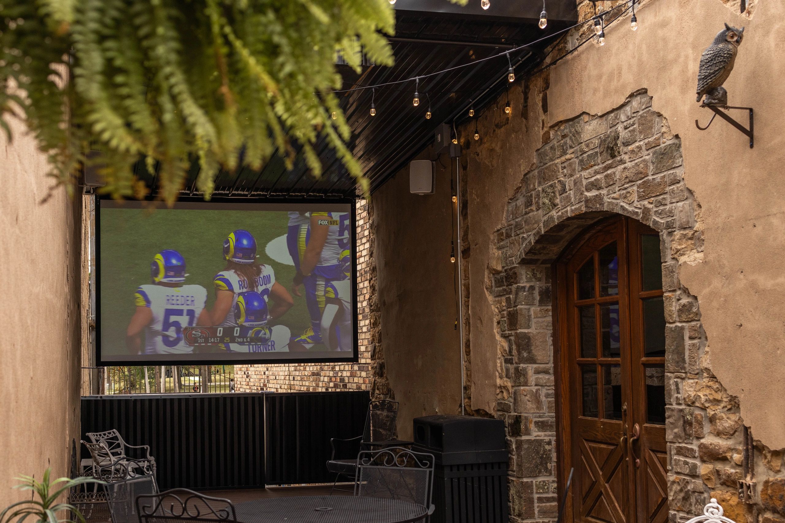 Outdoor seating area with TV screen showing a football game.