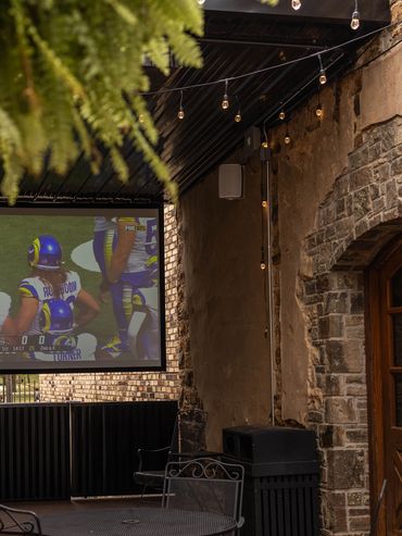 Outdoor seating area with TV screen showing a football game.