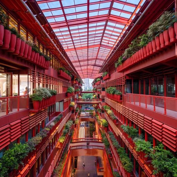 A vibrant red indoor corridor filled with green plants and a glass ceiling.