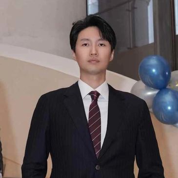 Two men in formal suits posing on a staircase with balloons in the background.