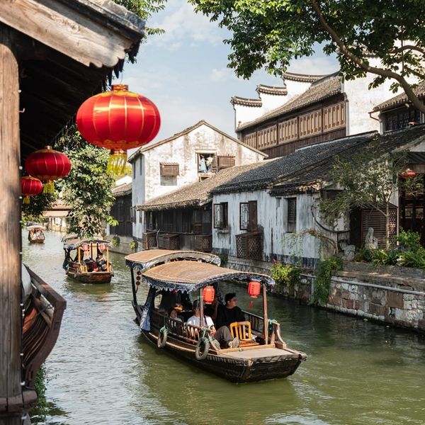 Traditional wooden boats float along a serene canal lined with old buildings and red lanterns.
