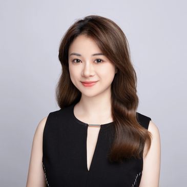 Professional young woman with long brown hair smiling in a black sleeveless top.