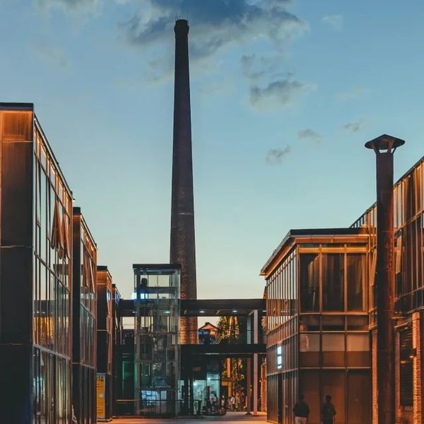 Evening view of modern buildings with a tall chimney in the background.