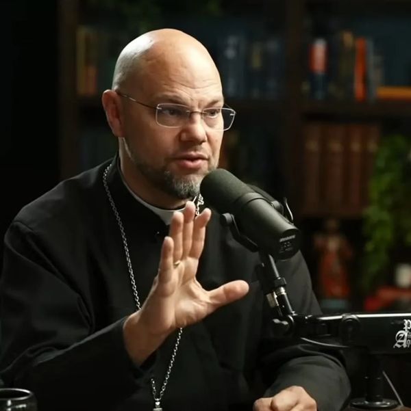 Bald man in religious attire speaking into a microphone during a podcast.