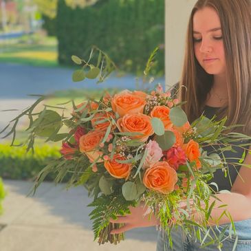 Young woman holding a vibrant bouquet of orange roses and greenery.